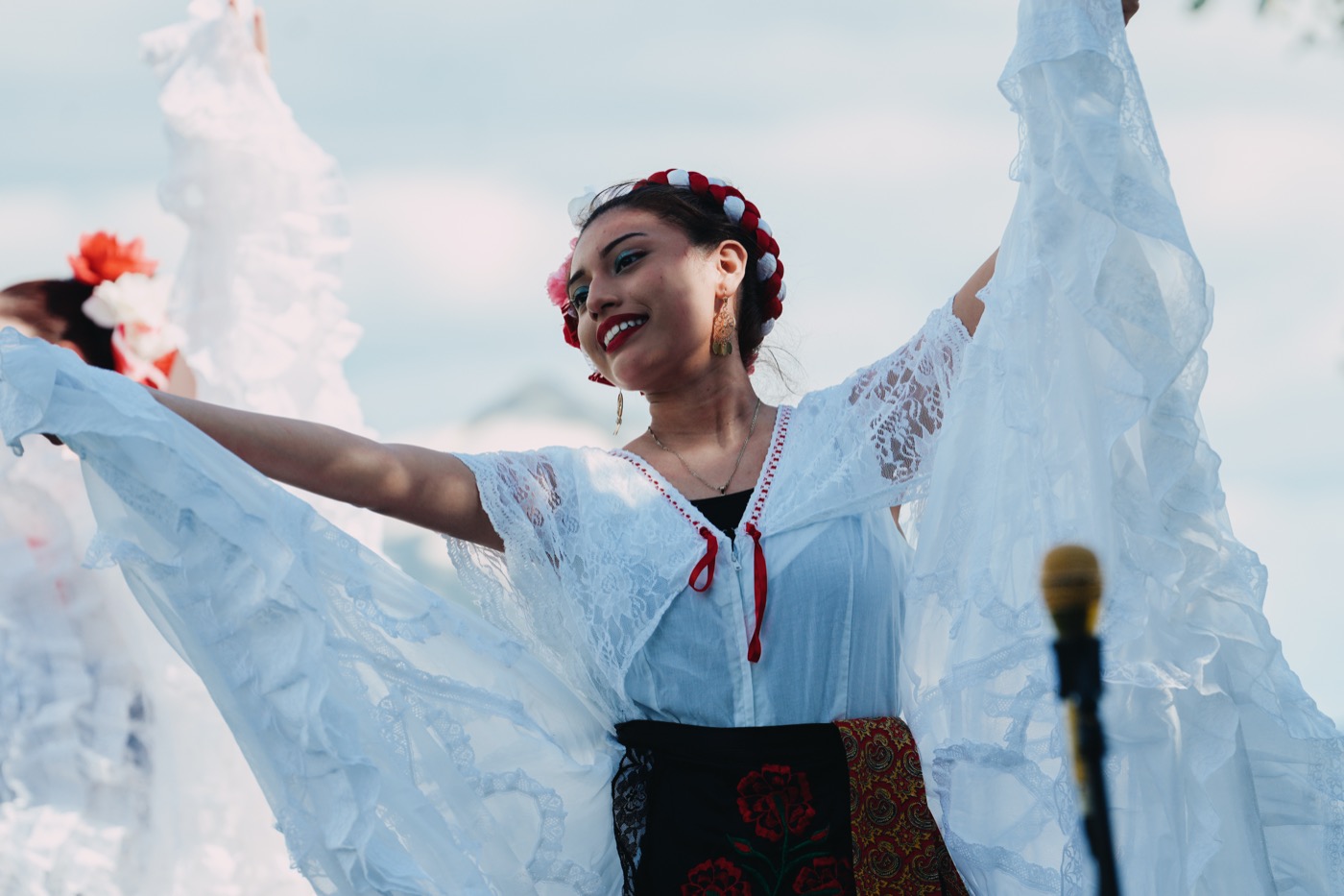 Ballet Folklórico dancer in flowing white lace arms outstretched, smiling on stage