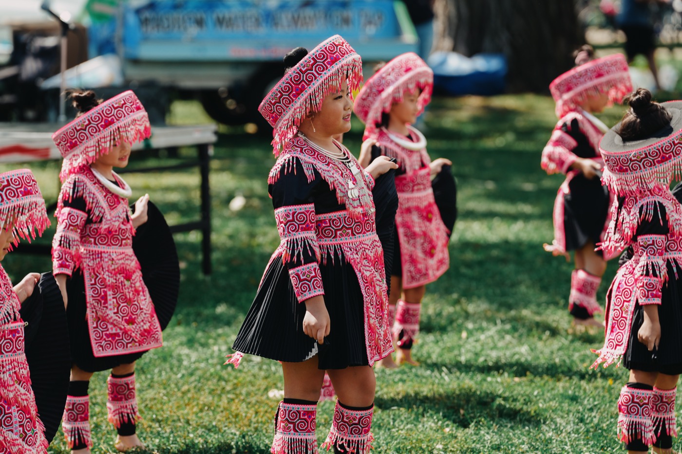 Hmong children in vibrant pink traditional costumes performing a cultural dance on stage