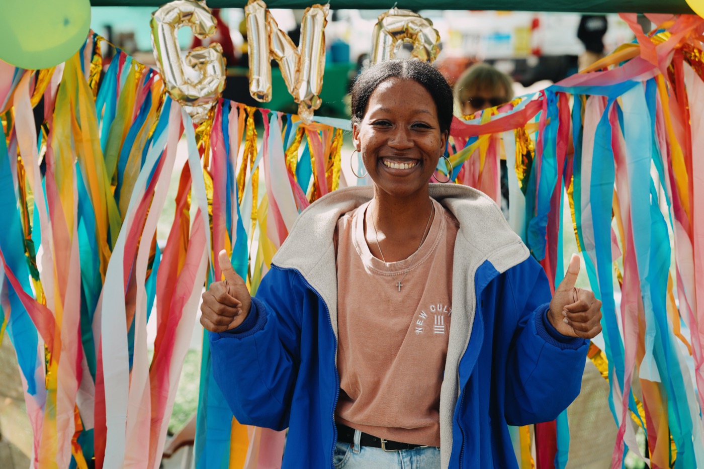 Community member giving a joyful thumbs-up in front of colorful GNG streamers and balloons